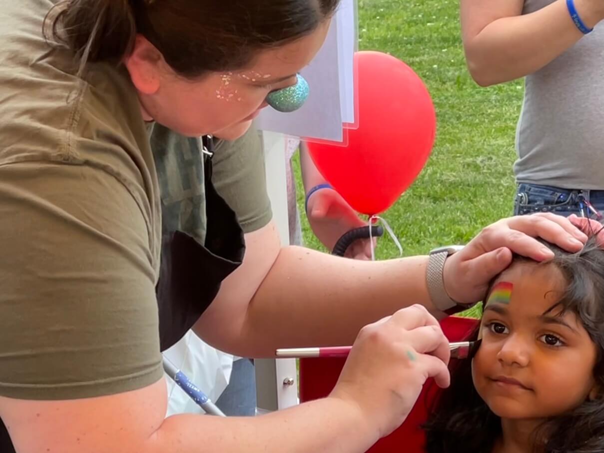 Girl with a rainbow flag painted on her cheek at an outdoor event