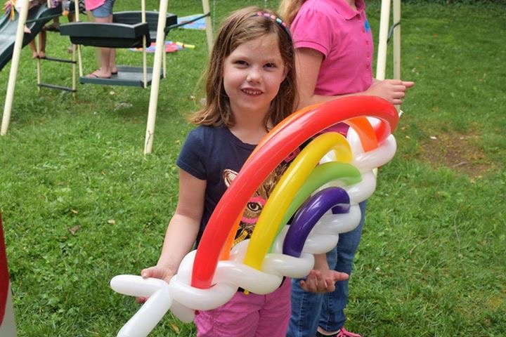 Girl holding a rainbow balloon sculpture in the grass