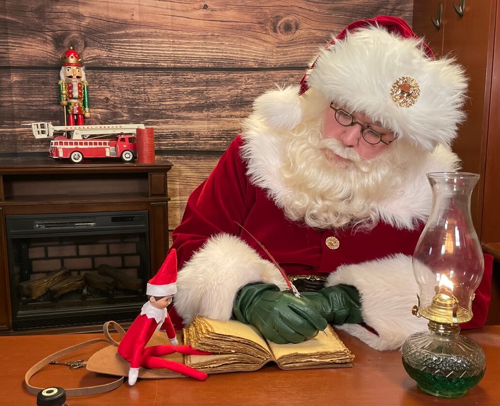 Santa writing in his nice list book by lantern light