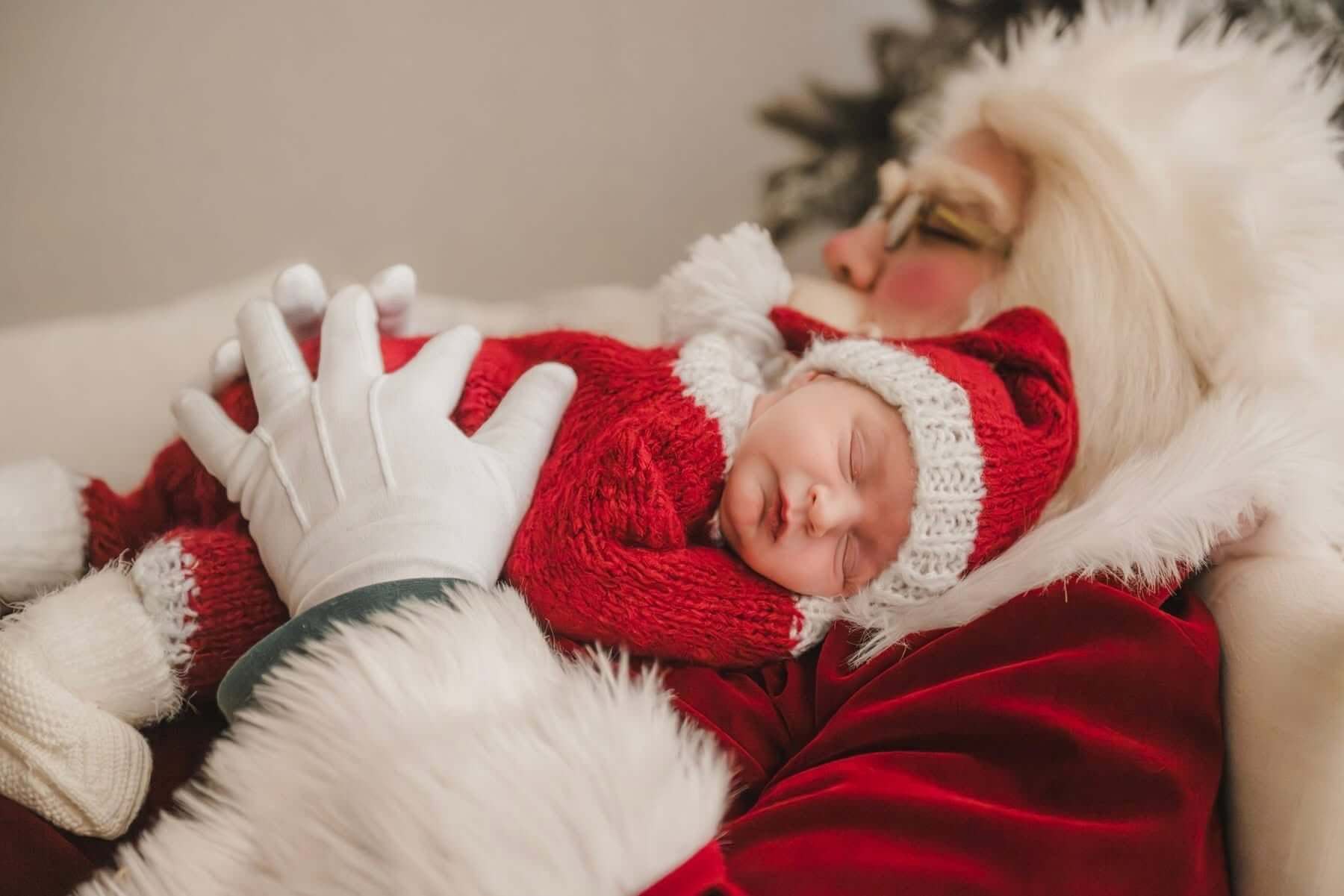 Santa tenderly cradling a sleeping newborn in red knits