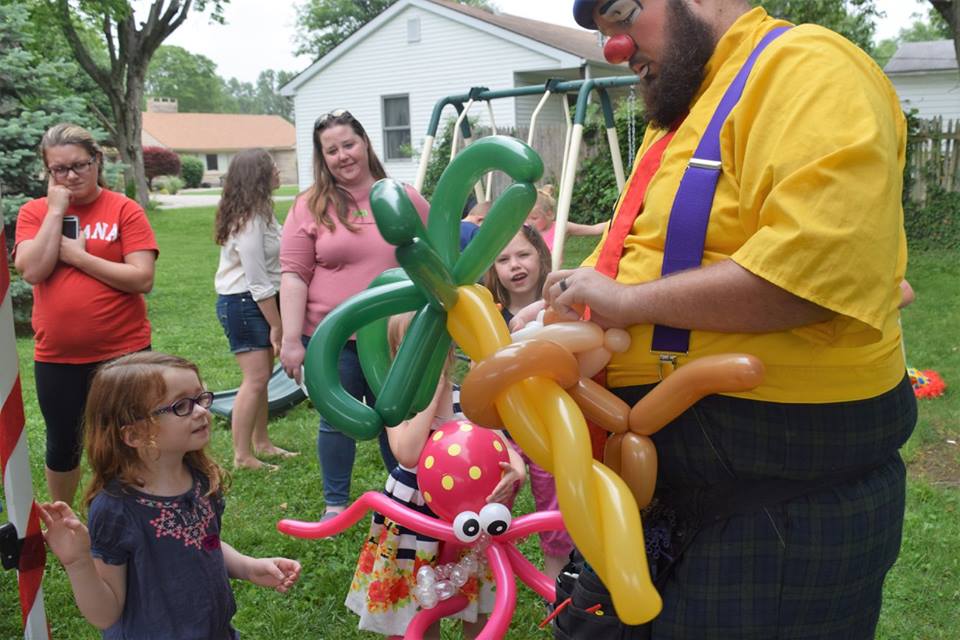 Big Top clown handing out a green and yellow balloon flower