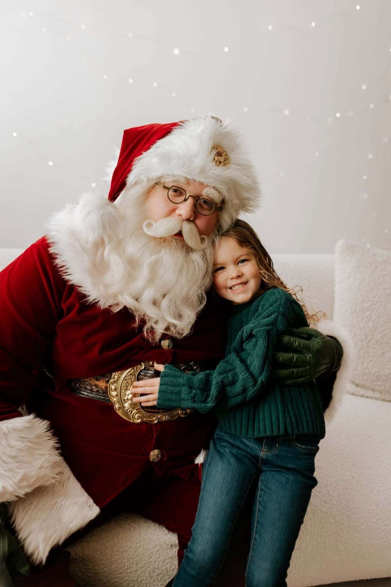 Santa hugging a smiling young girl in a green sweater