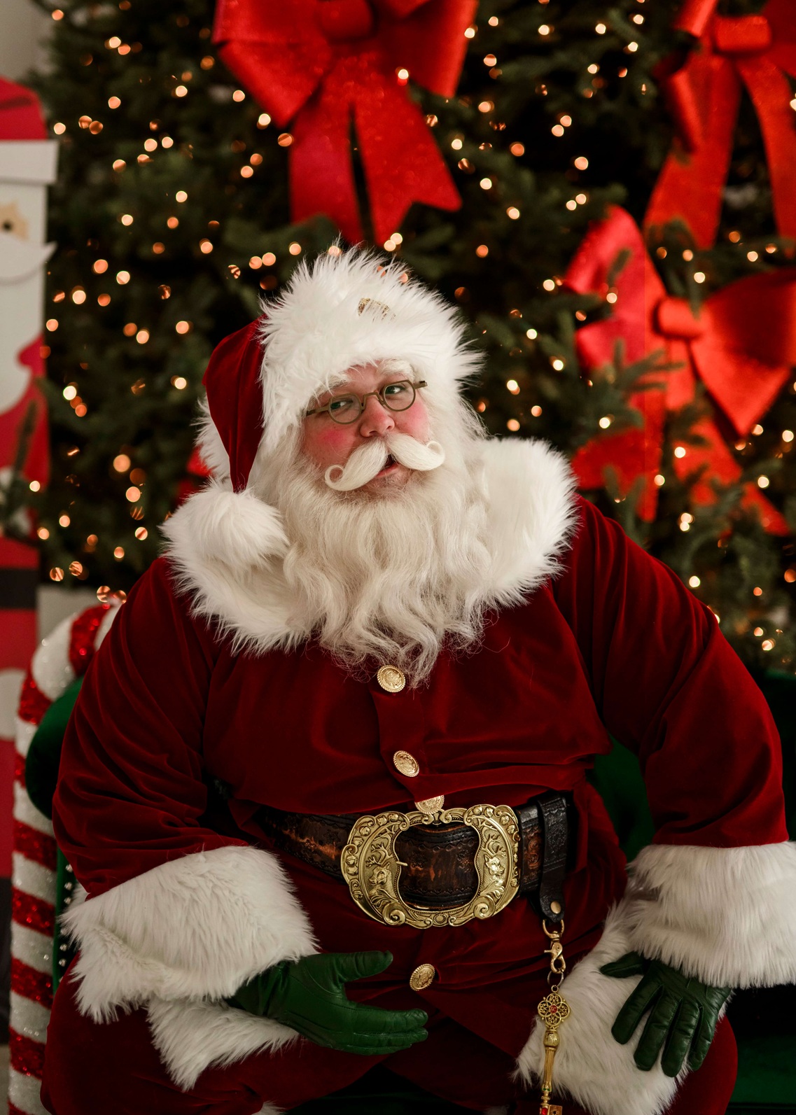Portrait of Santa in red velvet suit in front of a lit Christmas tree