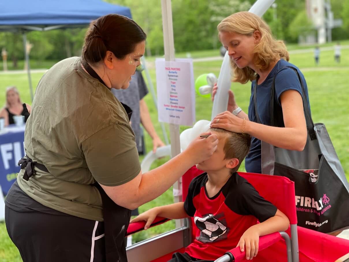 Face painter creating a design for a boy in a red chair