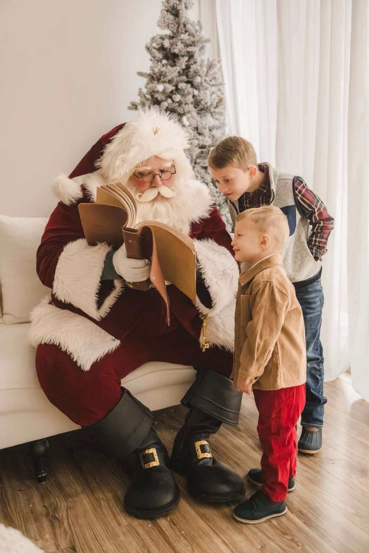 Santa reading his big book to two brothers by the tree