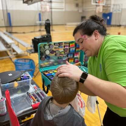 Face painter working with a child at an indoor gym event